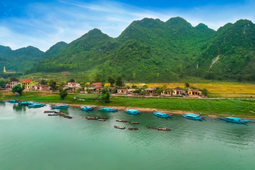 Blue wooden boats bring tourists on the big river in front of green mountains in Phong Nha   Ke Bang, a UNESCO World Heritage Site in Quang Binh Province, Vietnam